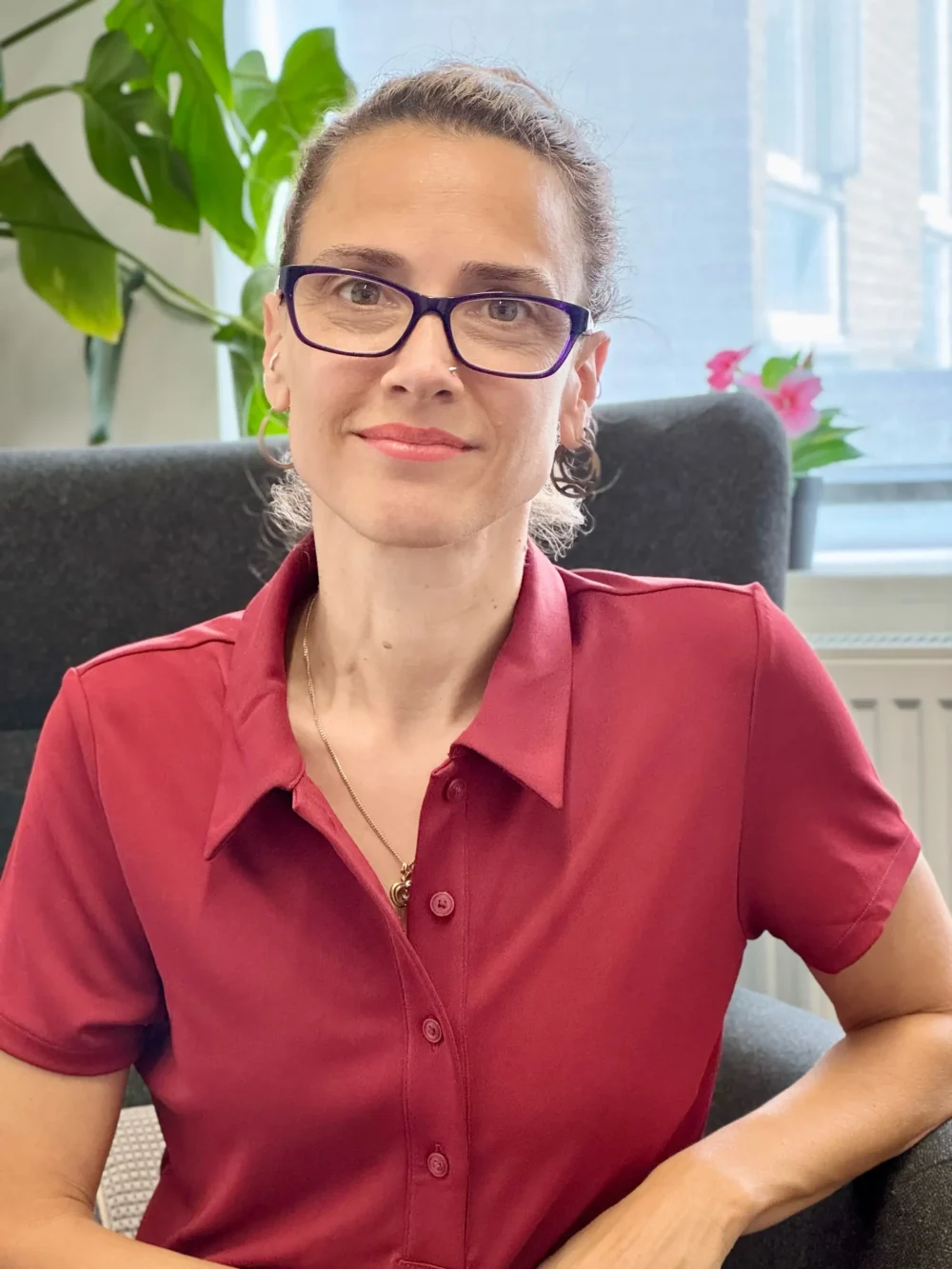 Friendly portrait of counsellor Paulina Filippou in a cozy office, dressed in a terracotta shirt with glasses